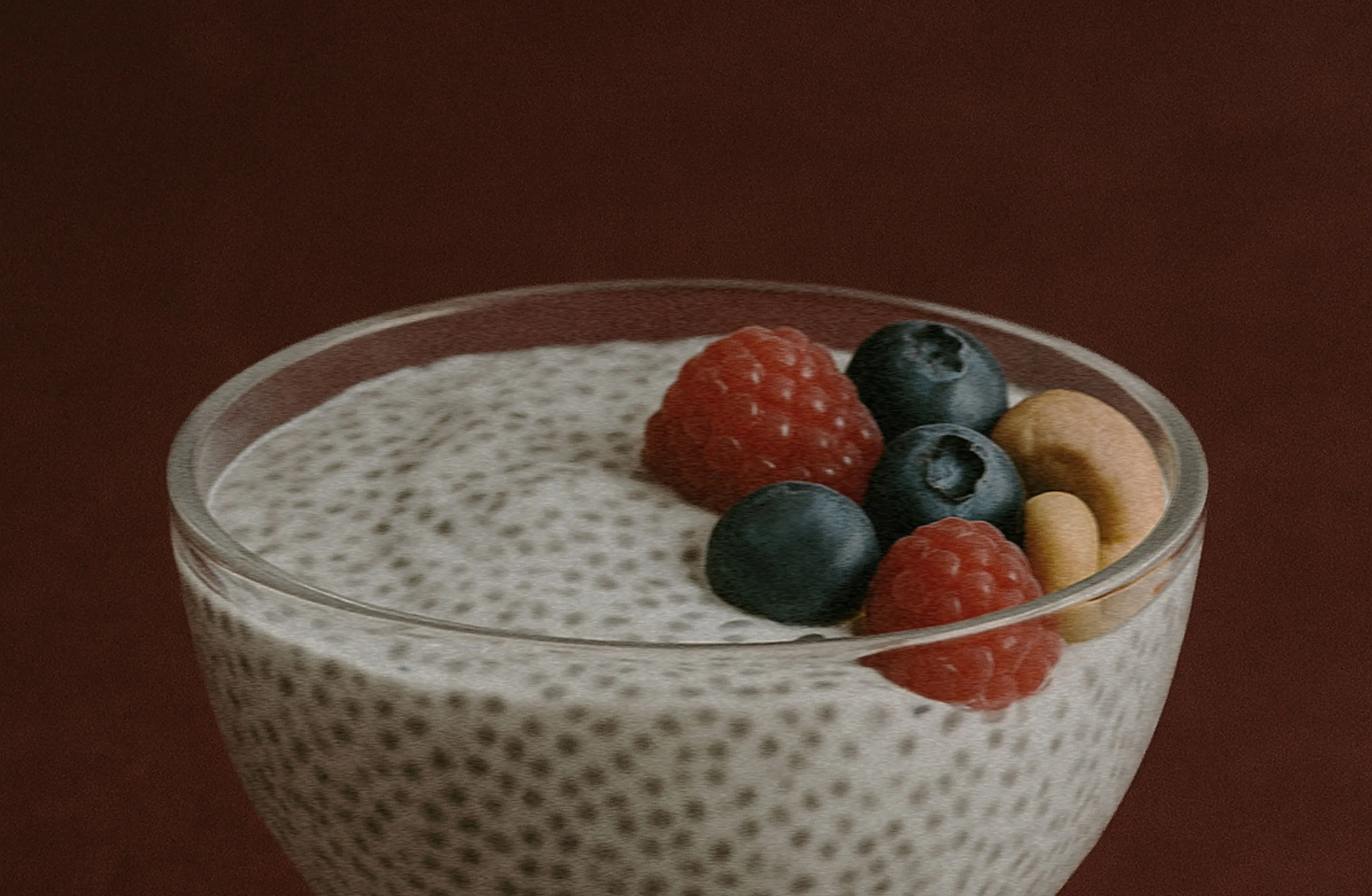 Glass bowl of chia pudding topped with raspberries, blueberries, and cashews set aganst a brown background.